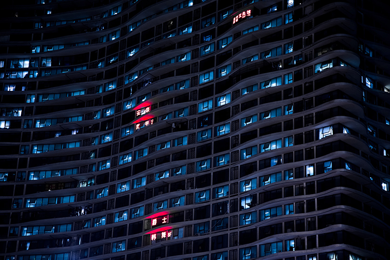 A high rise with several windows lit with blue light and two with red light.